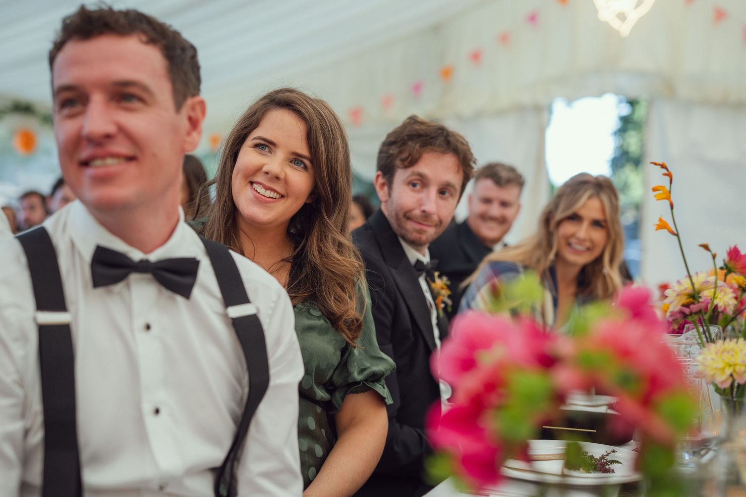 Smiling wedding guests seated at a reception table inside a white marquee tent at outdoor garden wedding reception in Co Meath.