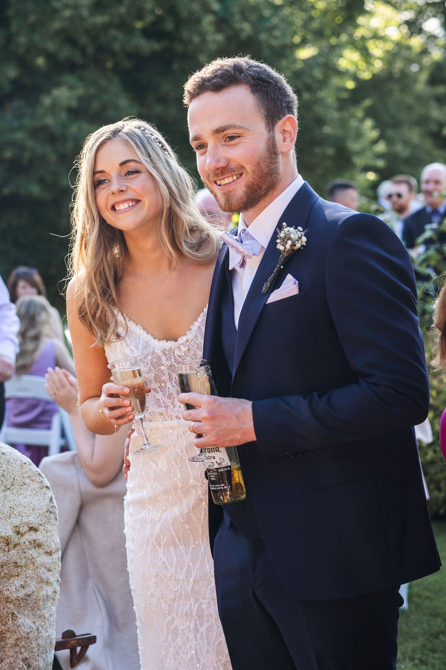Smiling bride and groom holding champagne glasses at outdoor wedding reception.