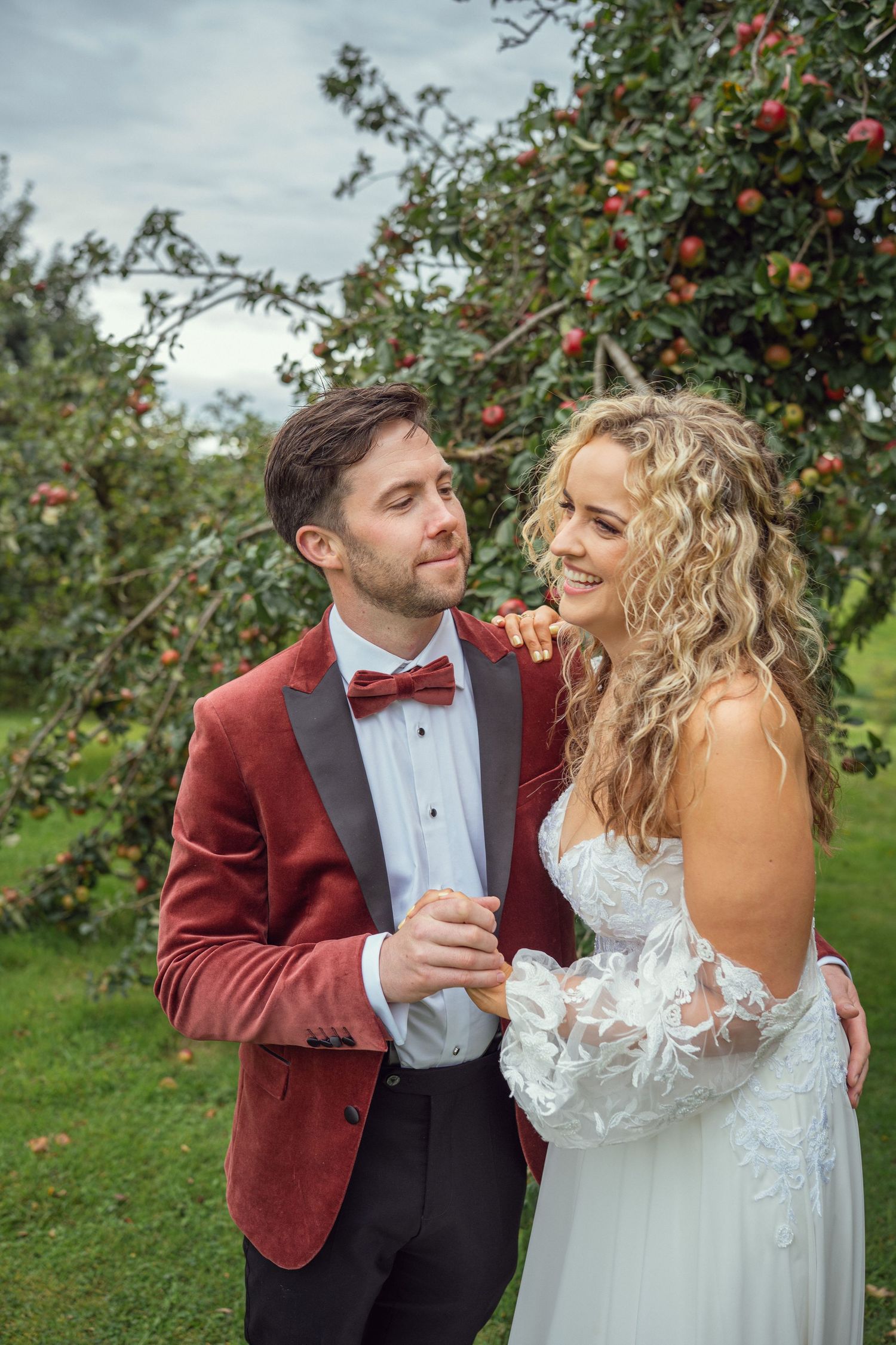 Smiling bride and groom in red velvet jacket sharing a tender moment outdoor garden wedding reception in Co Meath.