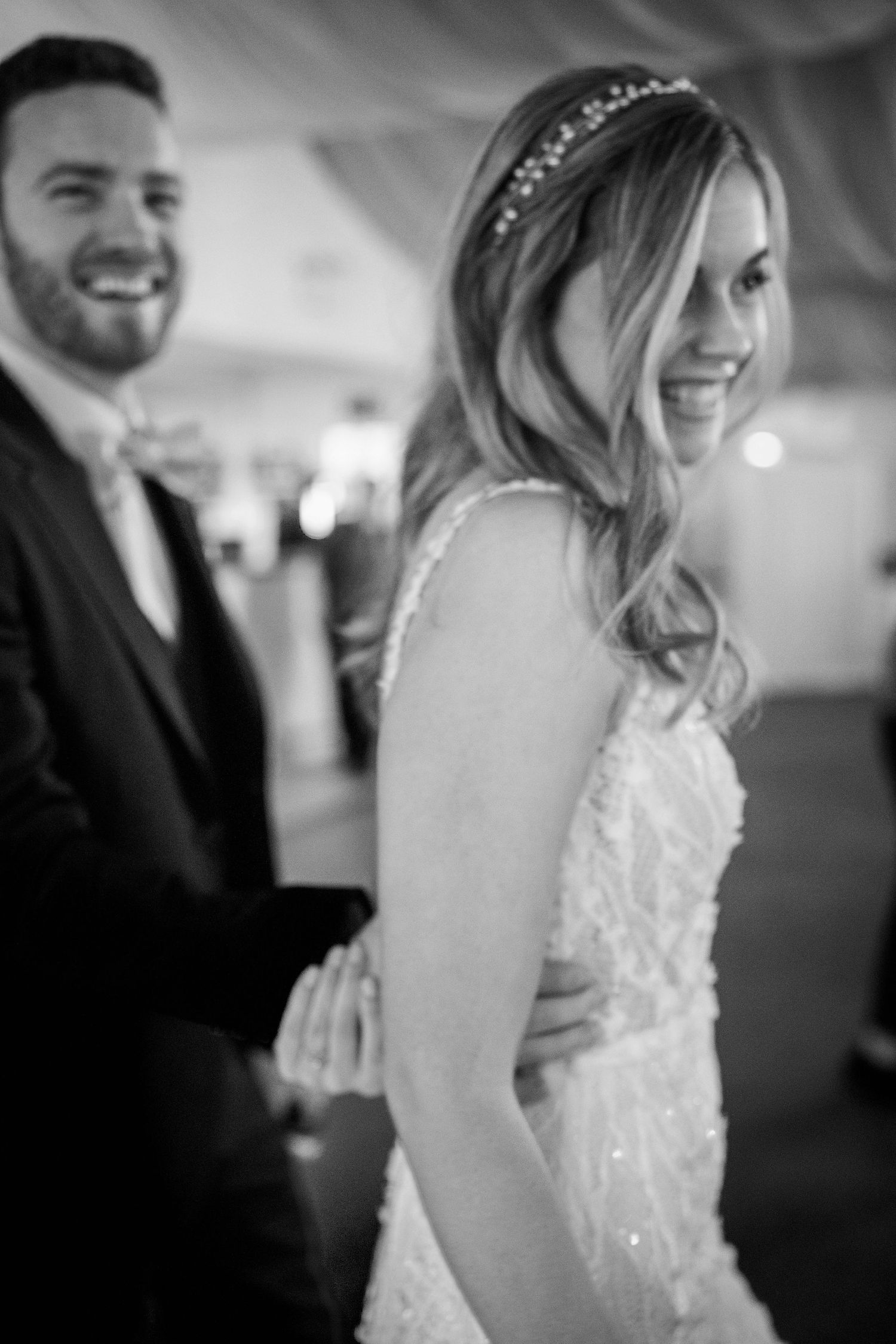 Black and white portrait of smiling bride in beaded gown with groom at wedding reception.