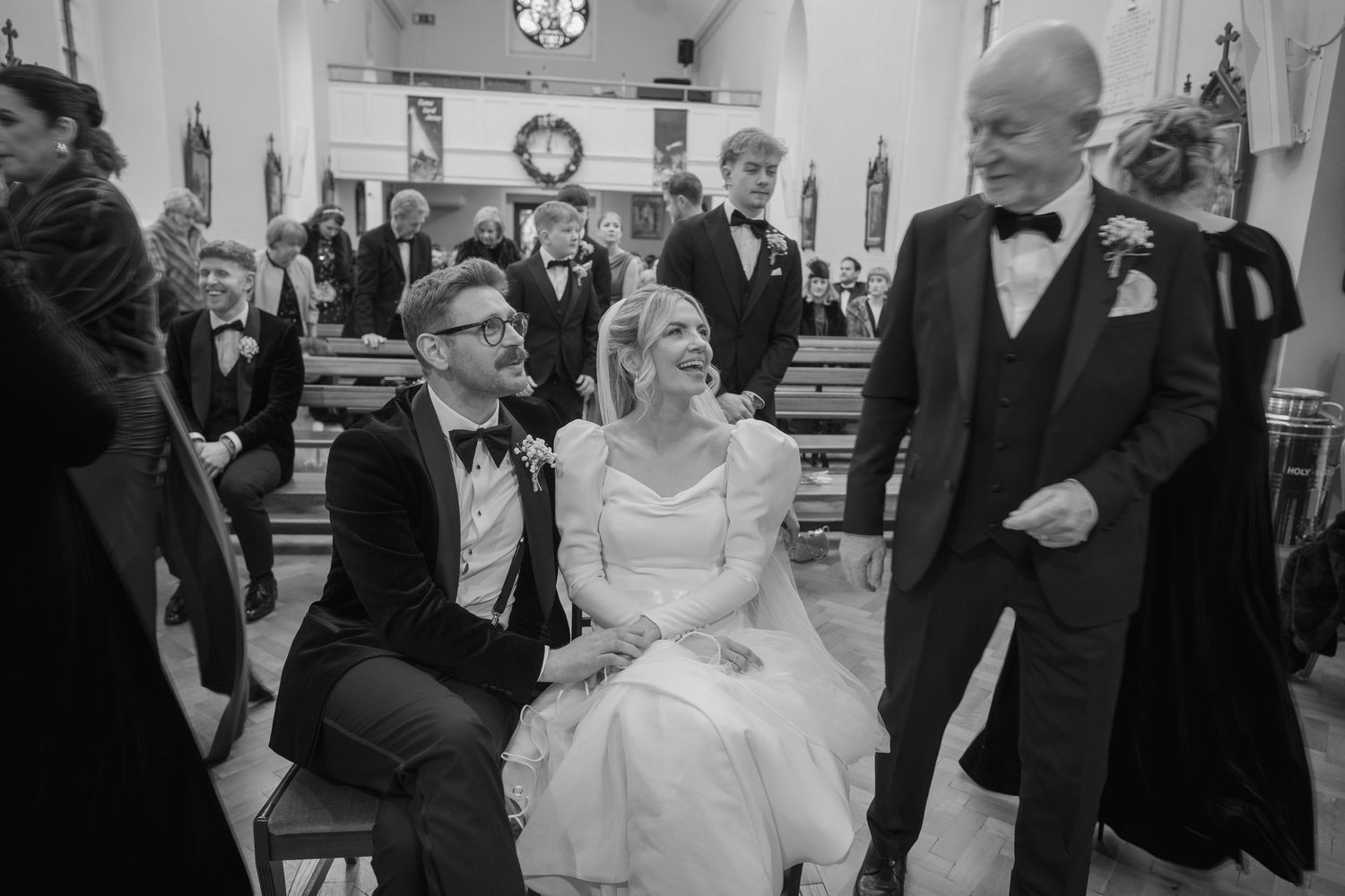 Bride and groom share a joyful moment seated in church aisle during wedding ceremony in black and white photo.