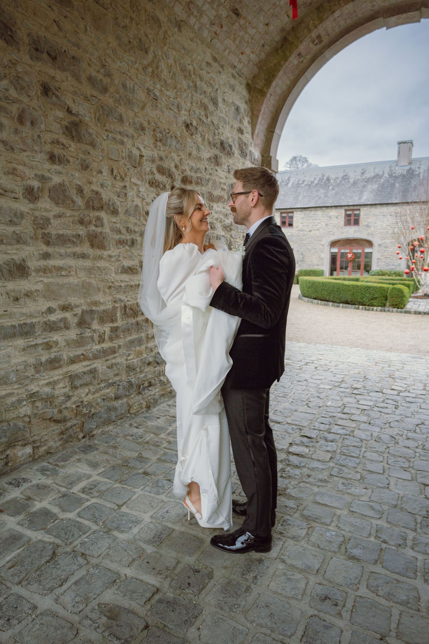 Bride and groom share a romantic moment under a stone archway at a historic venue on their wedding day.