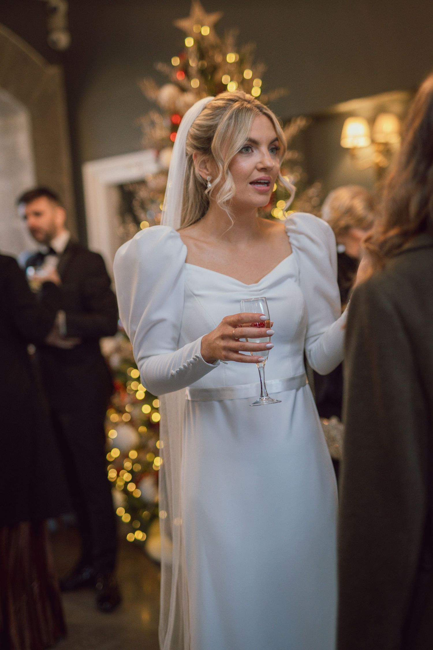 Bride in a white long-sleeve wedding gown holds a champagne glass at her wedding reception at Clonabreany House wedding in Meath