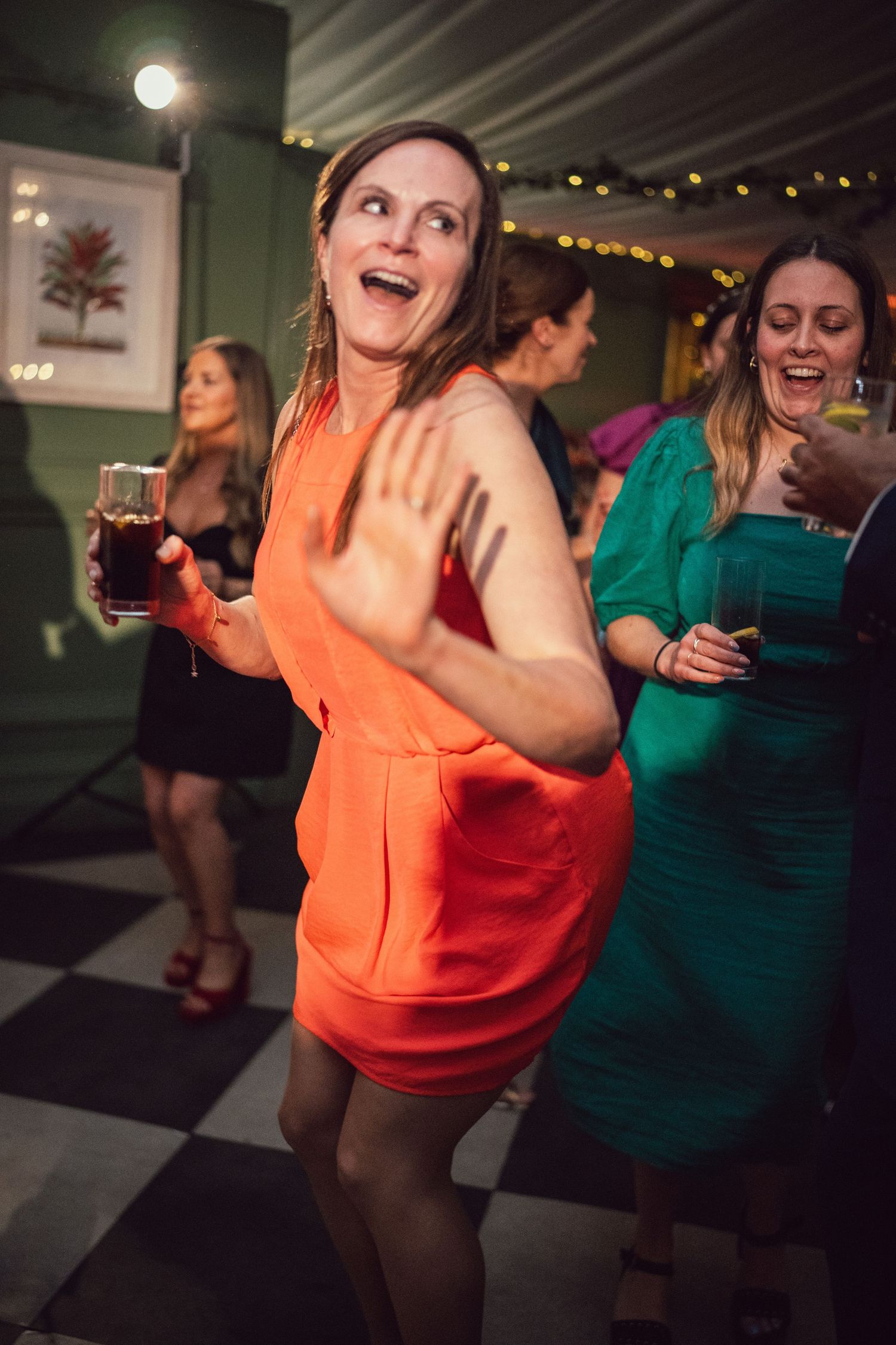 Woman in orange dress dancing joyfully at a wedding reception party.