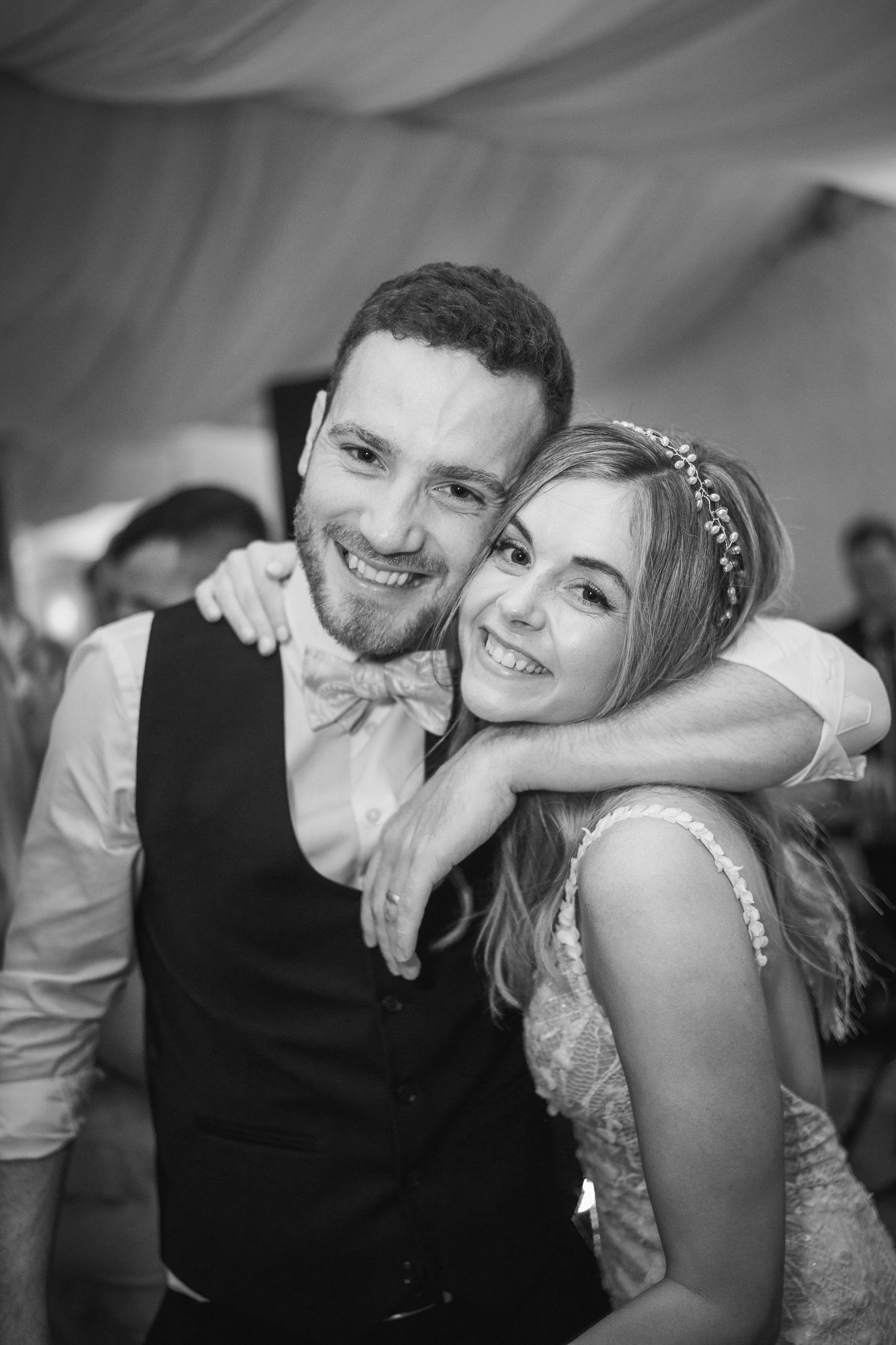 Black and white photo of a smiling bride resting her chin on the grooms shoulder during wedding reception.