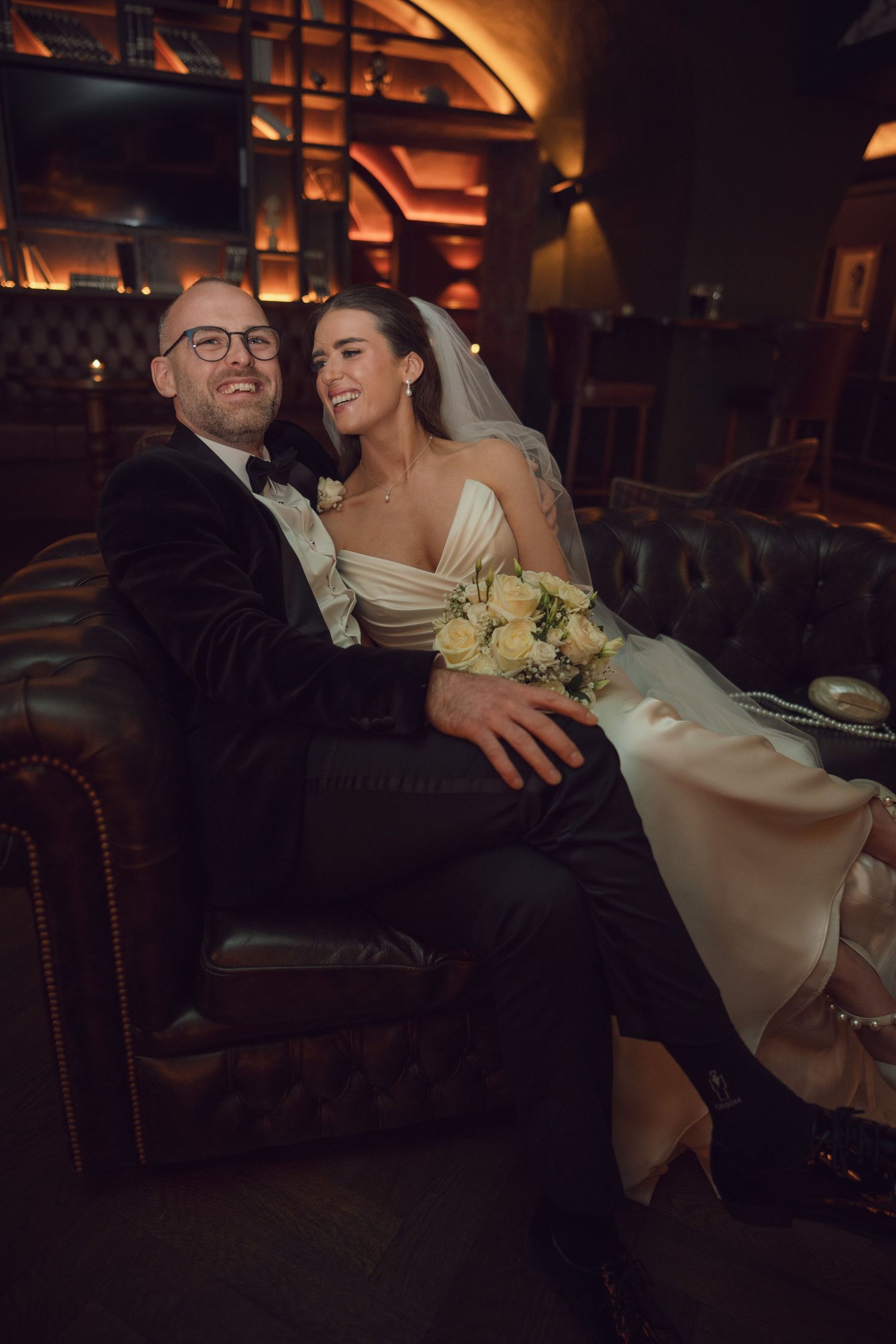 Bride and groom share a cozy intimate moment seated together on a leather sofa at the Manor House Mount Juliet wedding Kilkenny.