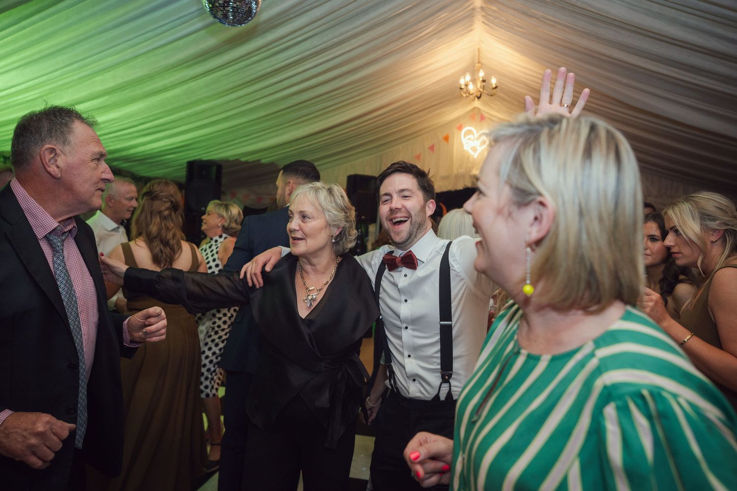 Wedding guests laugh and dance together under green lights at a lively evening wedding reception at garden wedding reception in Co Meath.