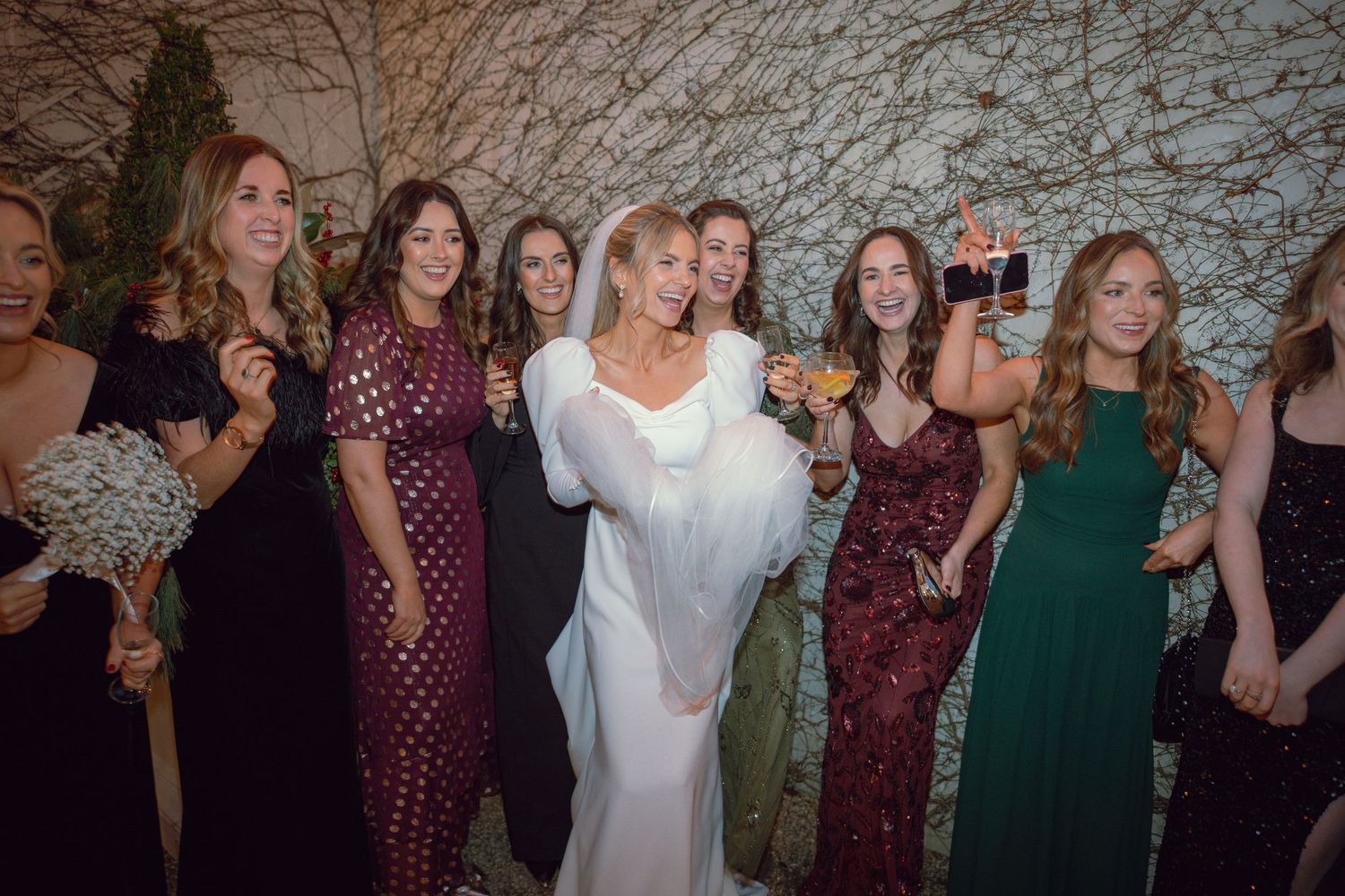 Bride in white gown celebrating with bridesmaids in colorful dresses at wedding reception.