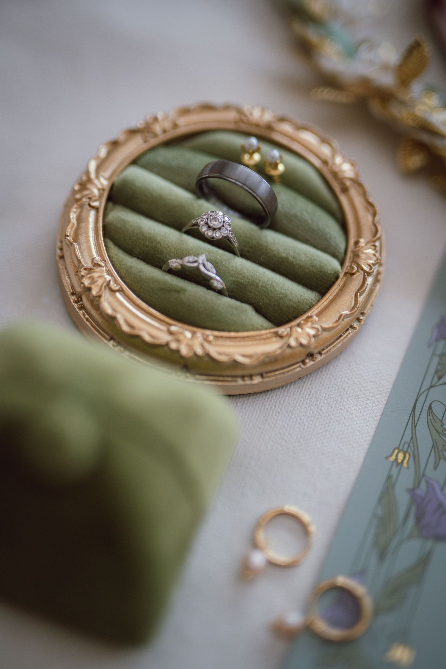 Three wedding rings displayed on green velvet oval ring box with ornate gold frame on white surface.