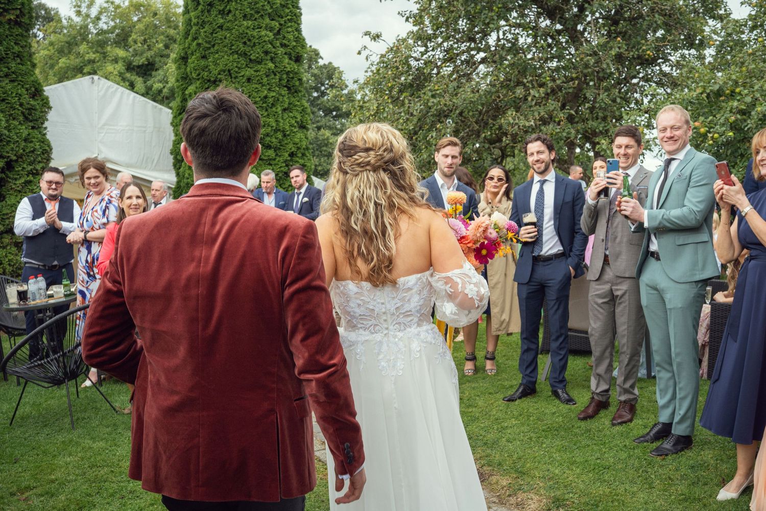 Bride and groom walk toward cheering guests during outdoor wedding reception at outdoor garden wedding reception in Co Meath.