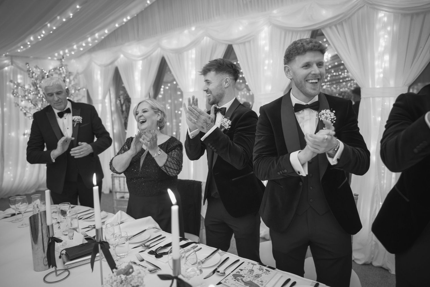 Wedding guests clapping and celebrating at a reception in a fairy light decorated marquee.
