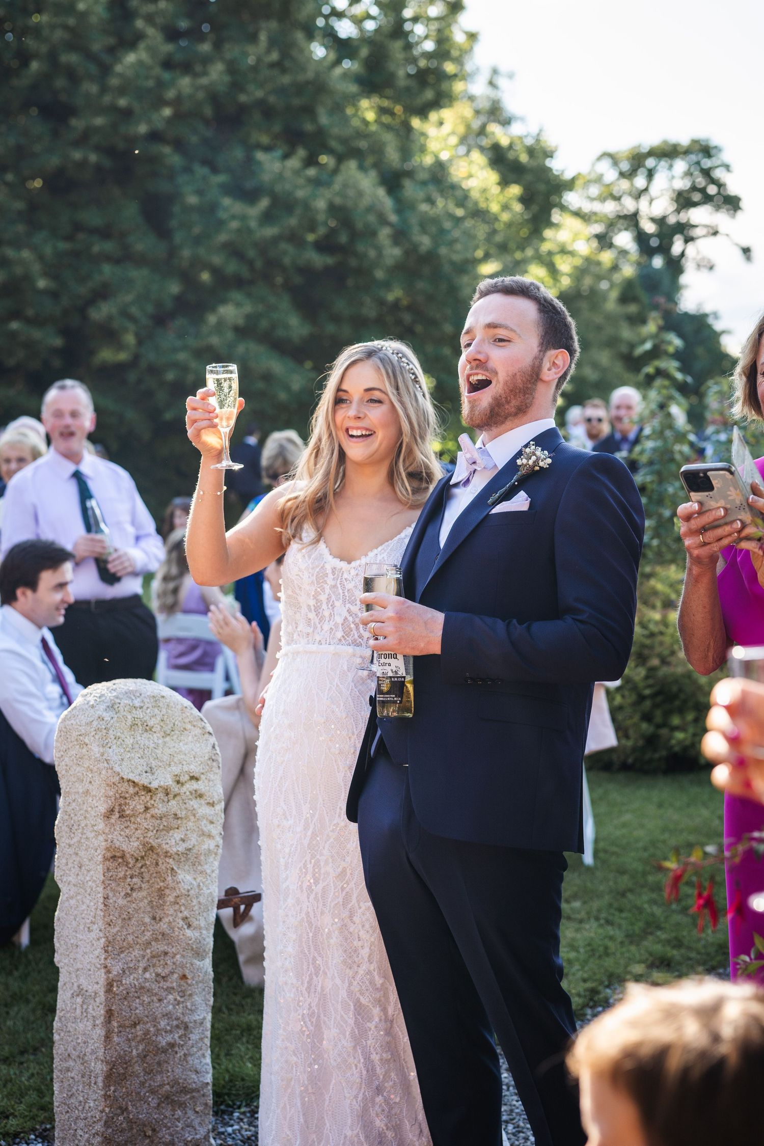 Joyful bride raising champagne glass with groom at outdoor wedding celebration.