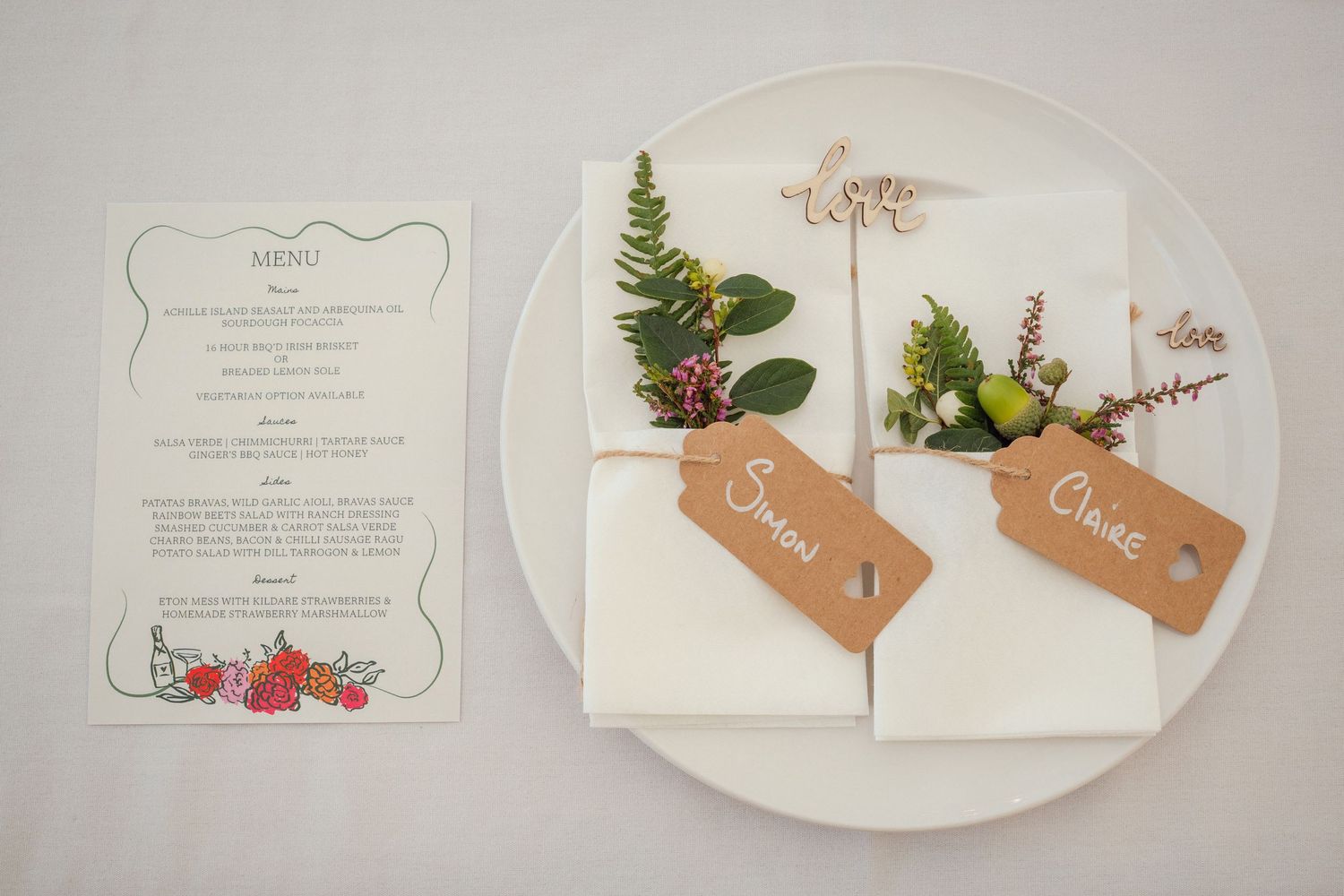 Elegant wedding place setting with kraft paper name tags, greenery, and illustrated menu card.