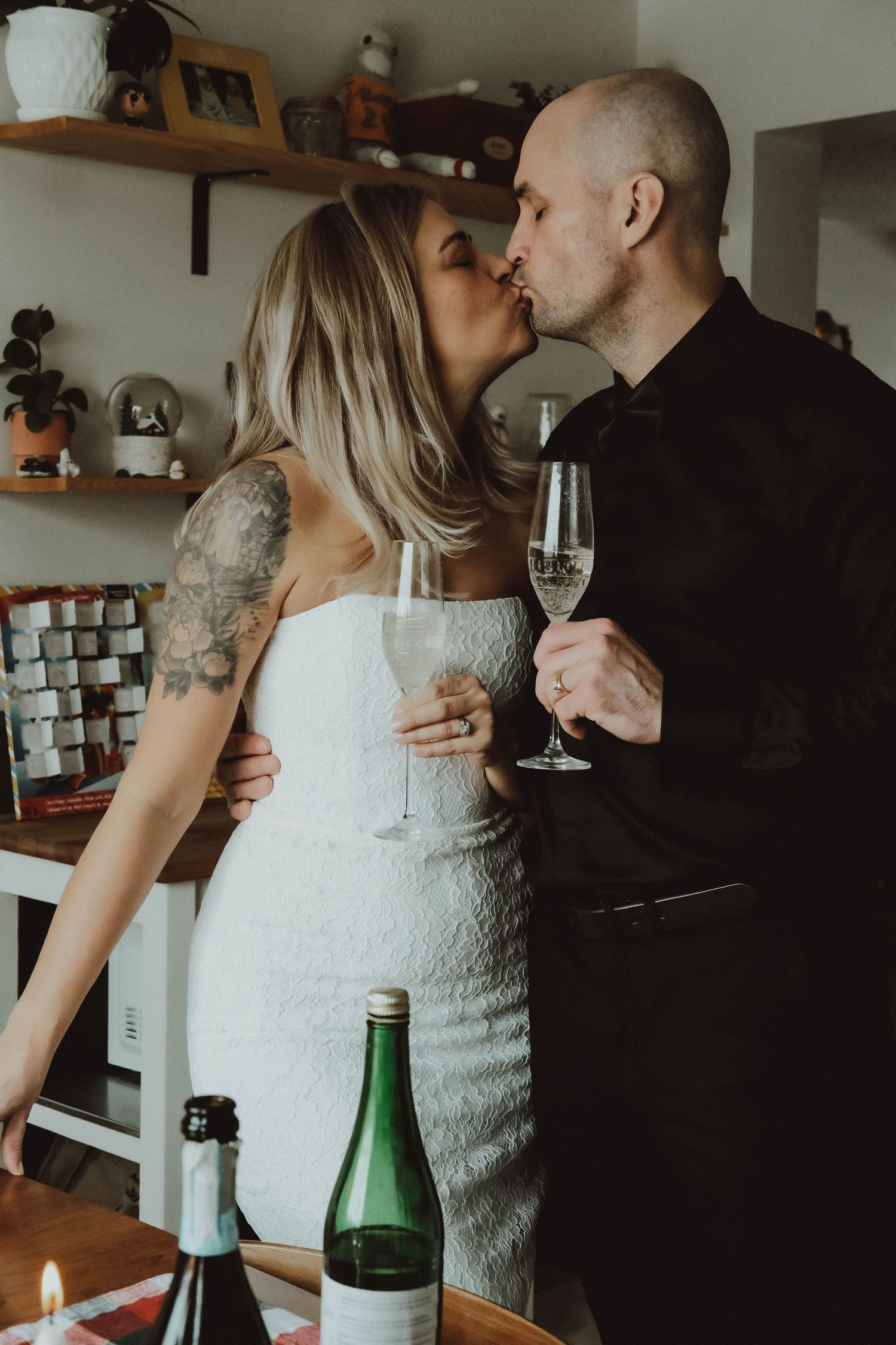 A couple shares an intimate kiss in their kitchen while holding champagne glasses during a romantic moment.
