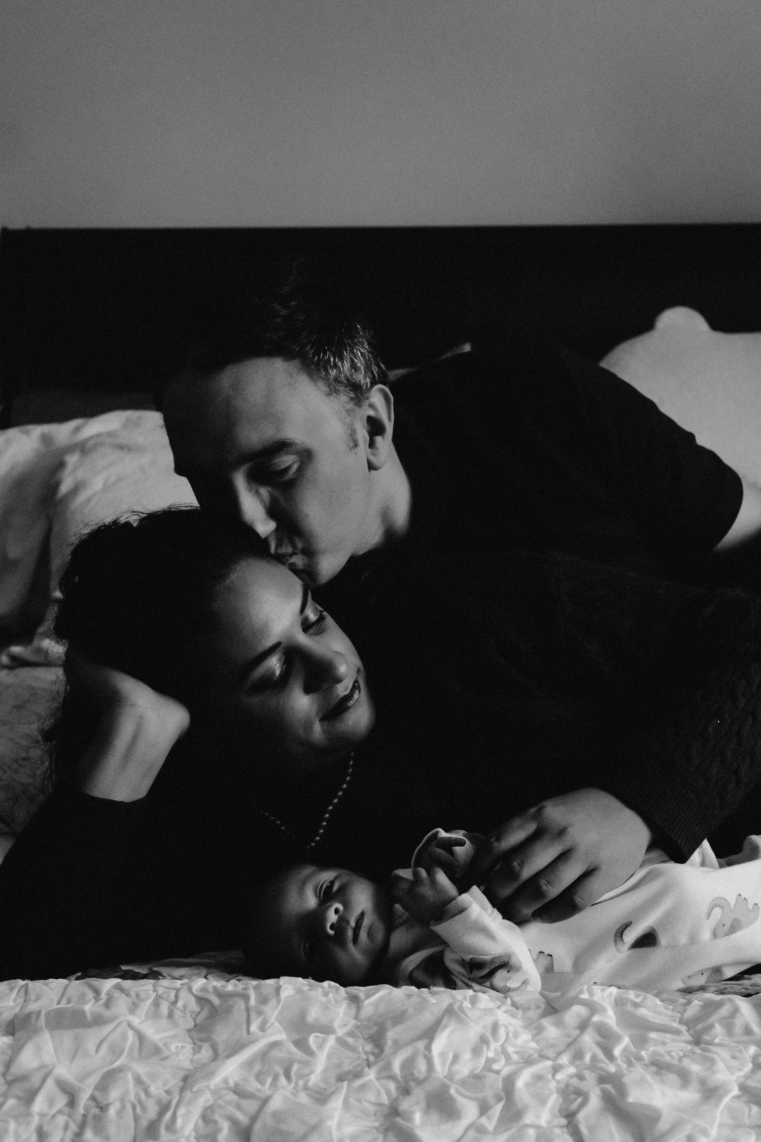 A romantic black and white photo series showing an intimate couple lying together on white bedding.