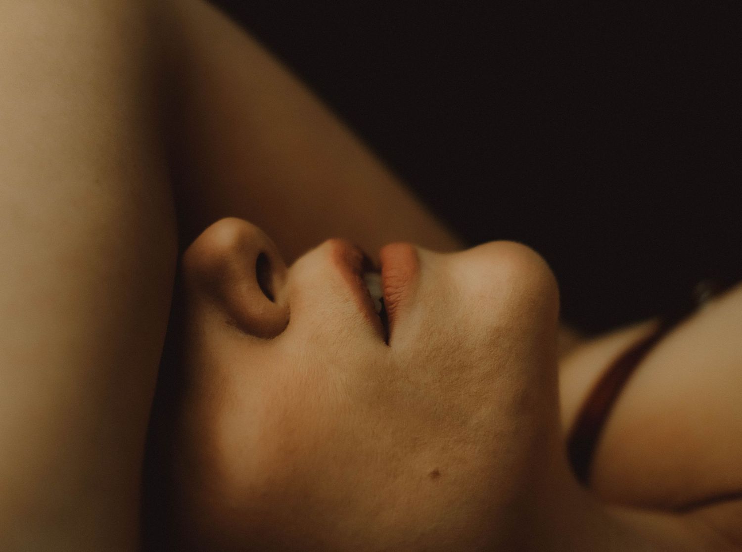 Close-up artistic portrait of a person's neck and jawline against a dark background.