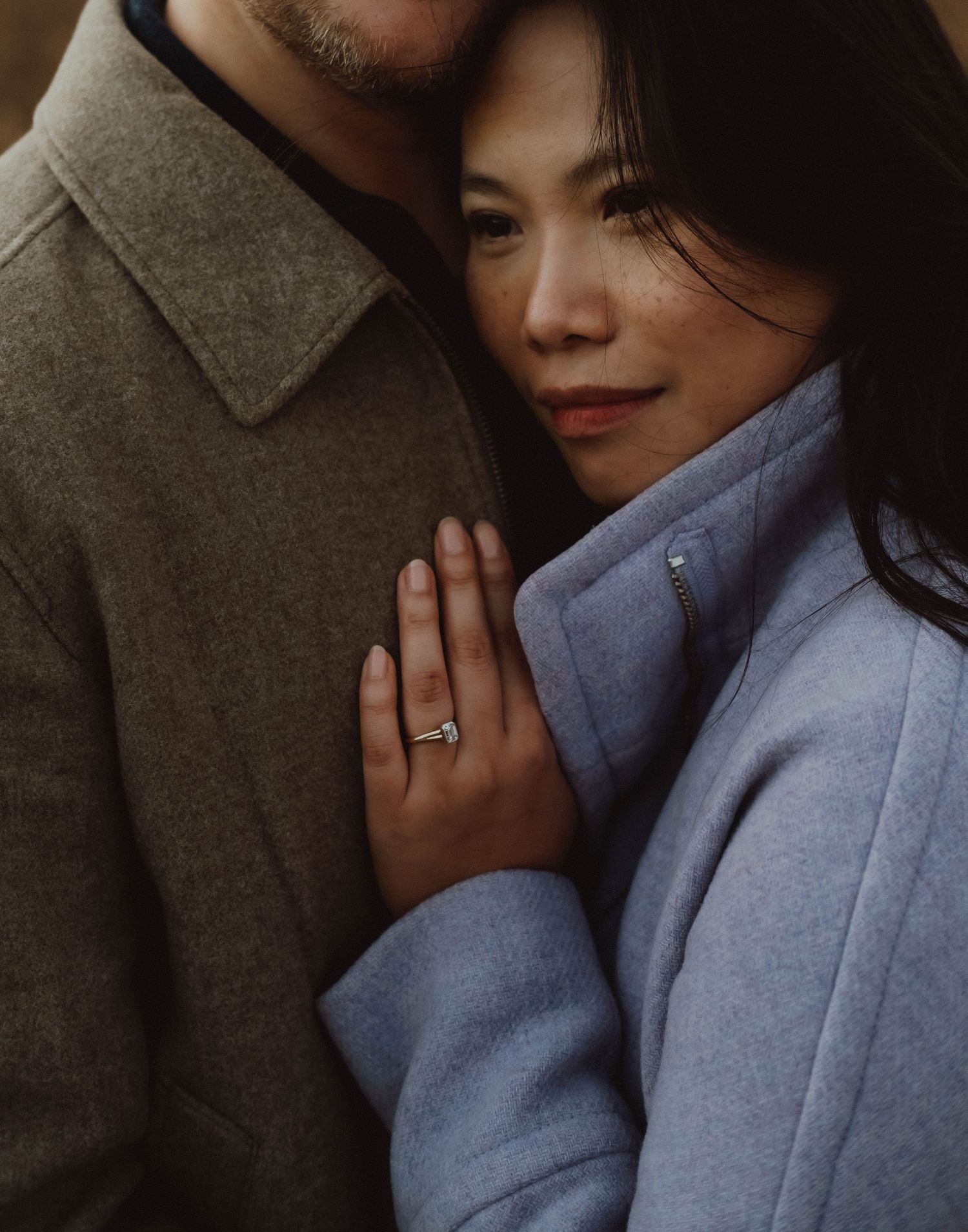 A romantic couple embraces intimately while wearing winter coats in a moody atmospheric setting.
