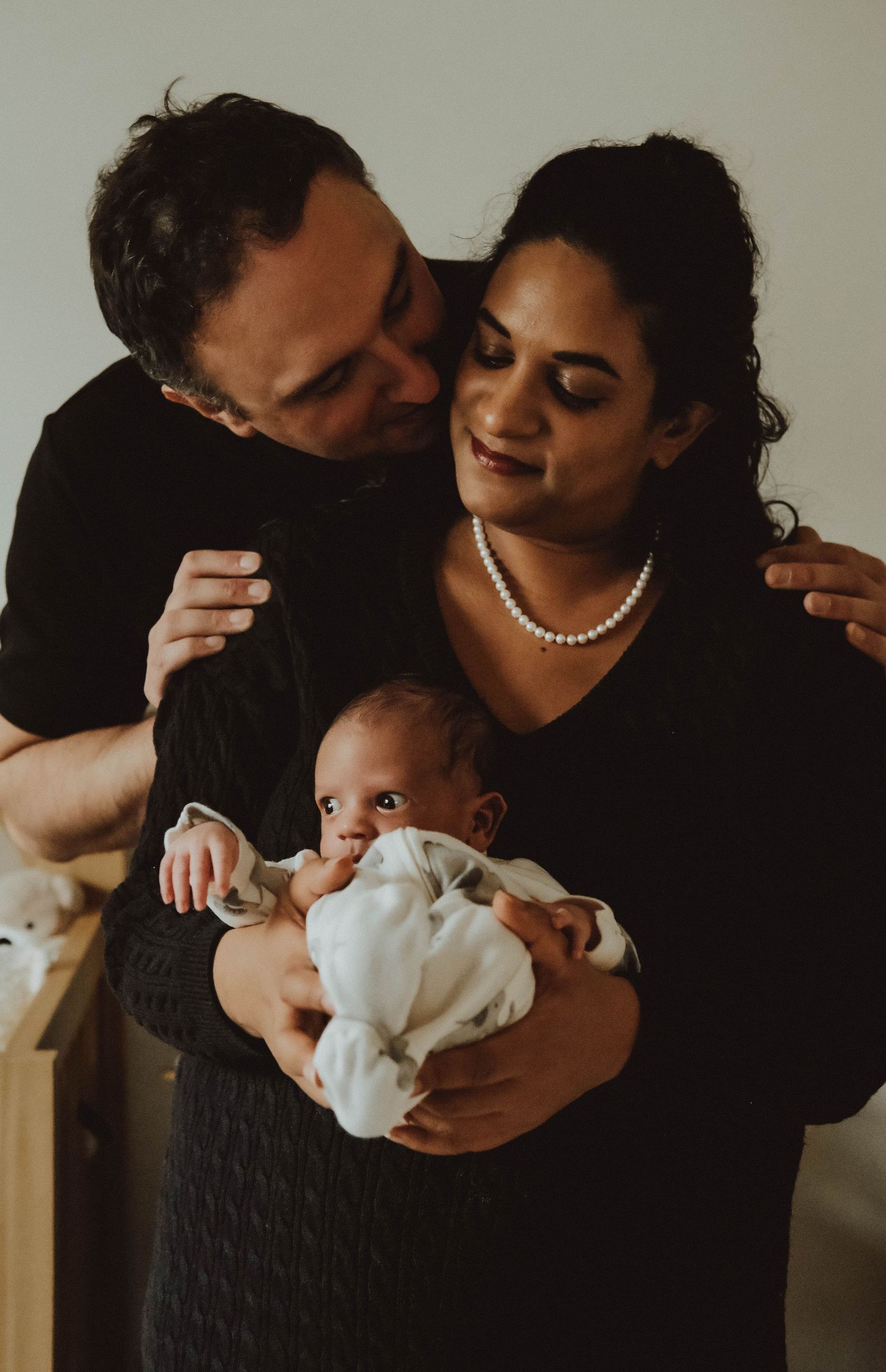 A loving couple cradles their newborn baby in a series of intimate dark-toned photographs.