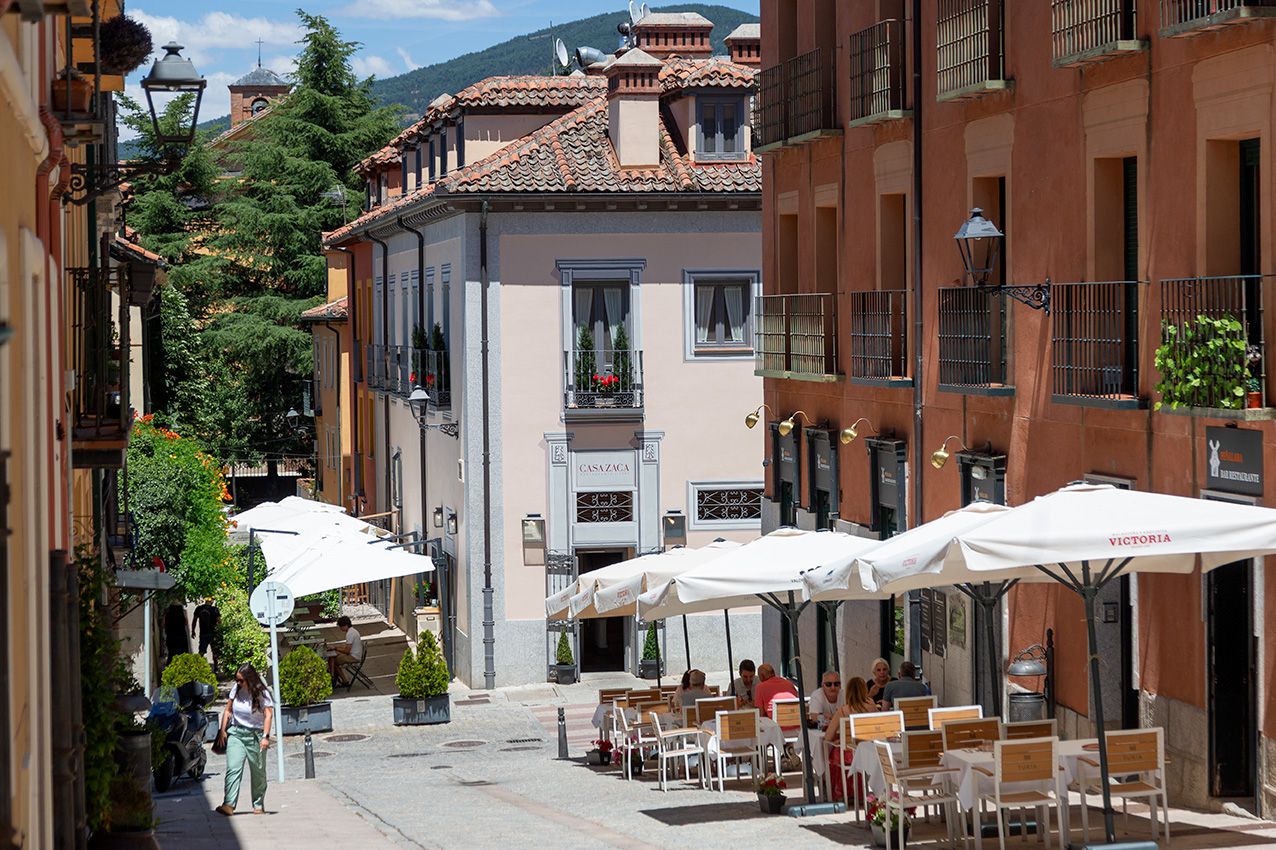Charming outdoor cafe with white umbrellas on a sunny European cobblestone street lined with colorful buildings.