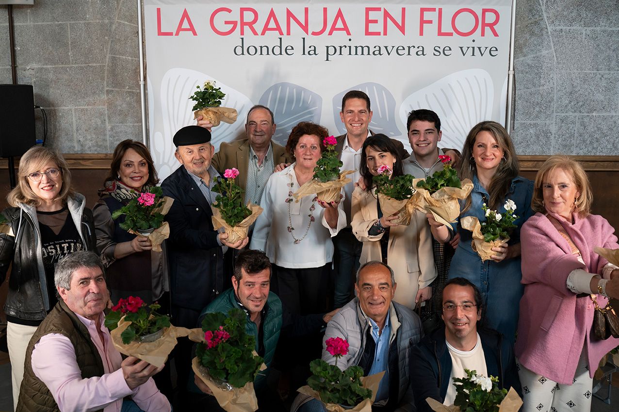 Group of people holding flowers and plants at La Granja en Flor spring event backdrop.