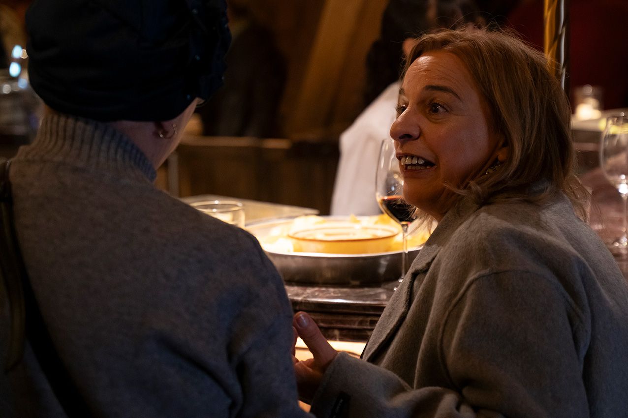 A woman holding a wine glass engages in an animated conversation at a cozy indoor dining event.