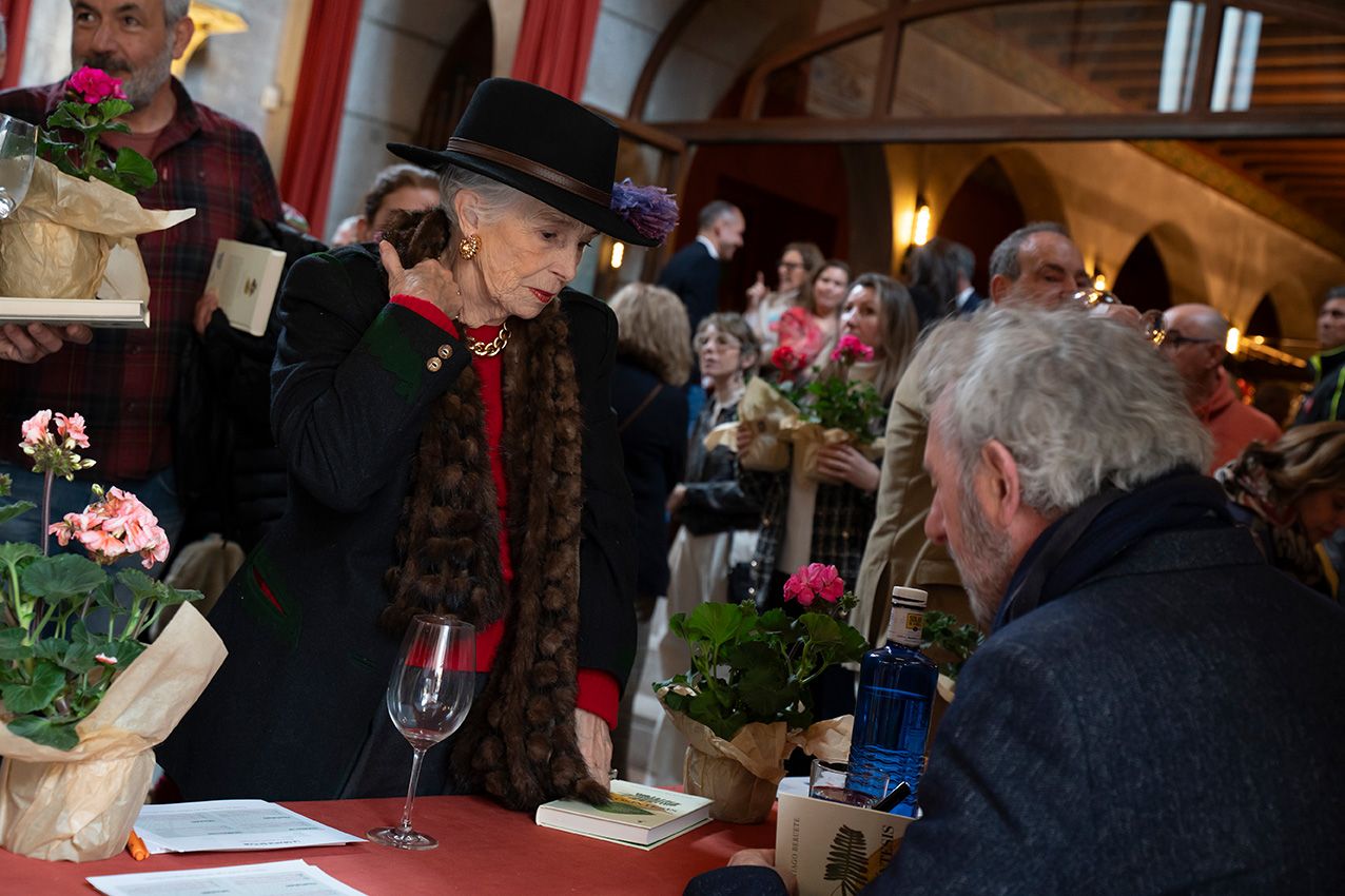 Woman in black hat conversing at table with potted flowers at La Granja en Flor event.