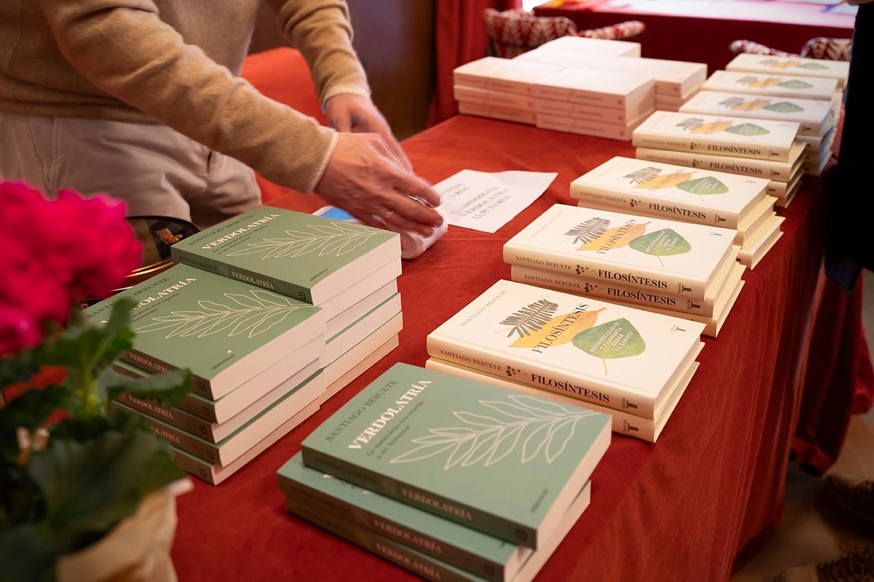 Stacks of green and white books displayed on red tablecloth at a book fair or literary event.