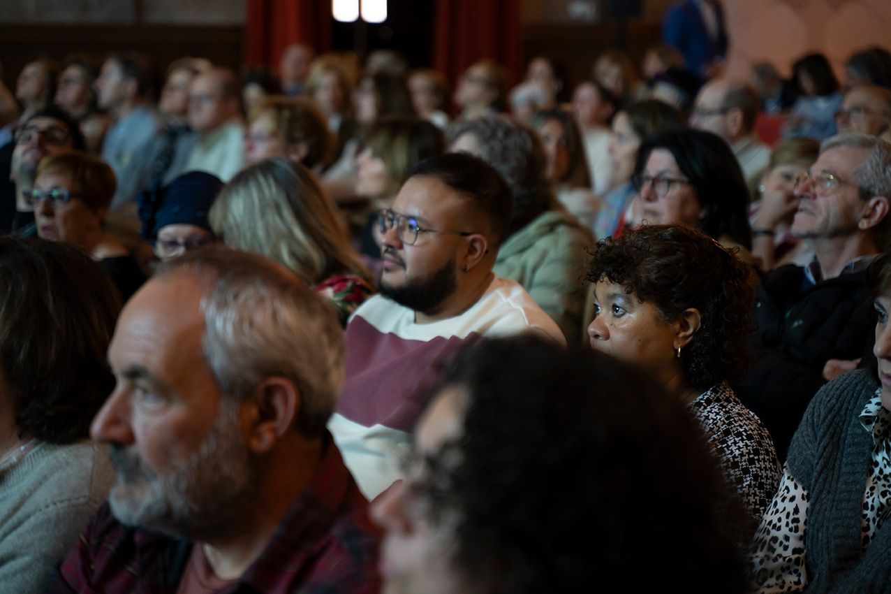 Diverse crowd of attentive audience members seated closely together at an indoor cultural event.