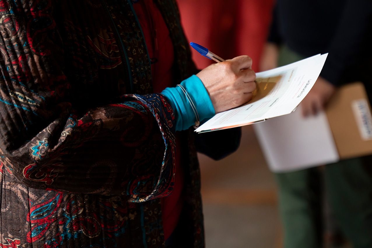 Person in colorful patterned jacket holding white paper and pen at an indoor event.