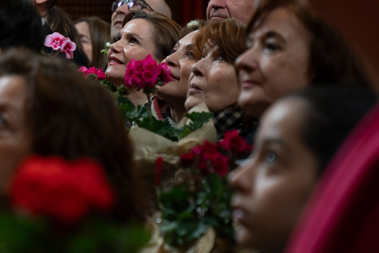 Crowd of people holding red and pink roses looking upward during an indoor floral event or ceremony.