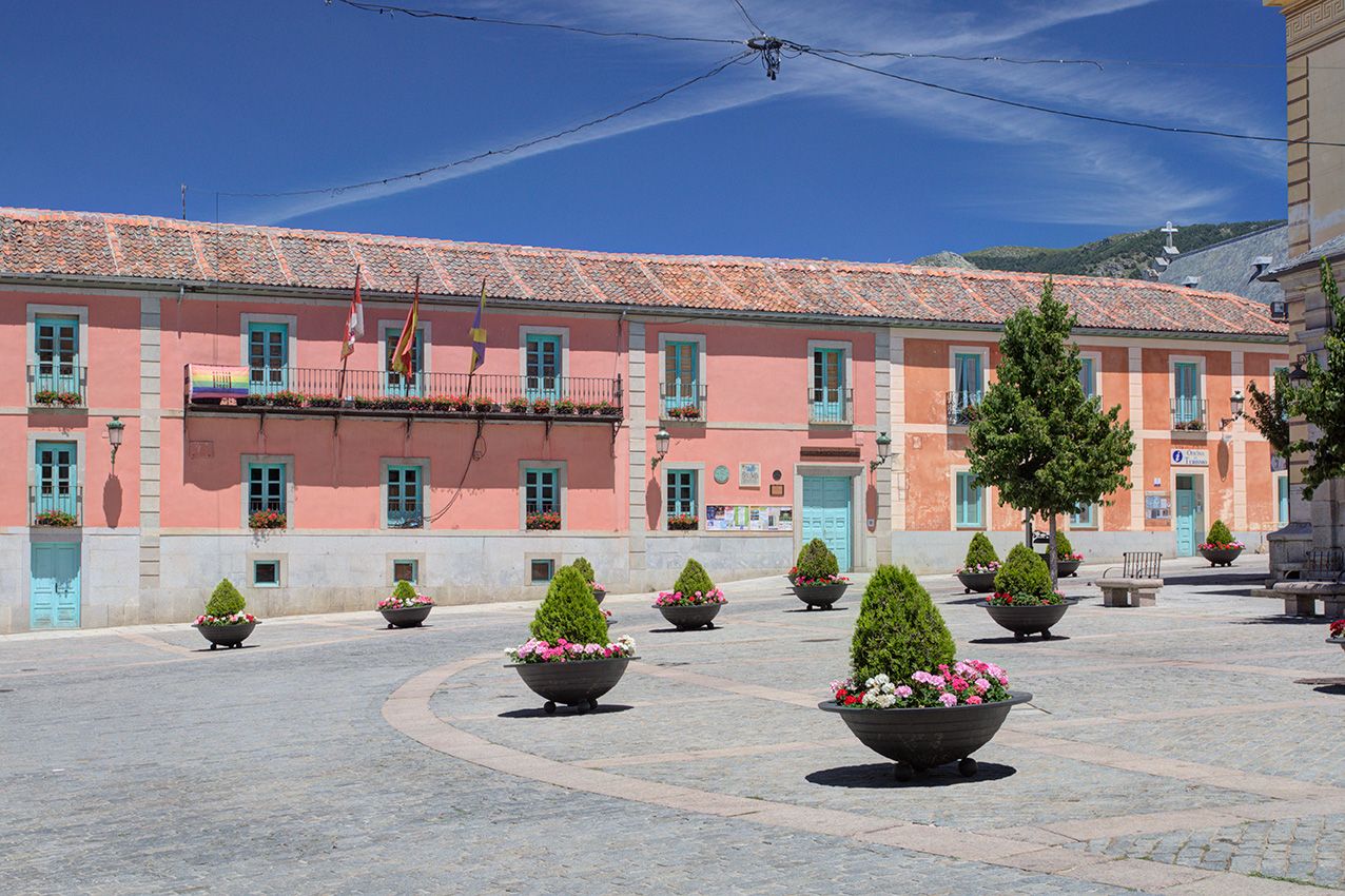 Pink municipal building with decorative potted trees in a sunny Spanish town square plaza.