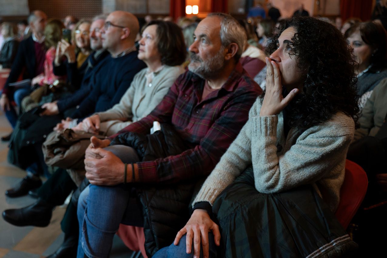 Engaged audience seated in red chairs watching a live event or presentation in a historic venue.
