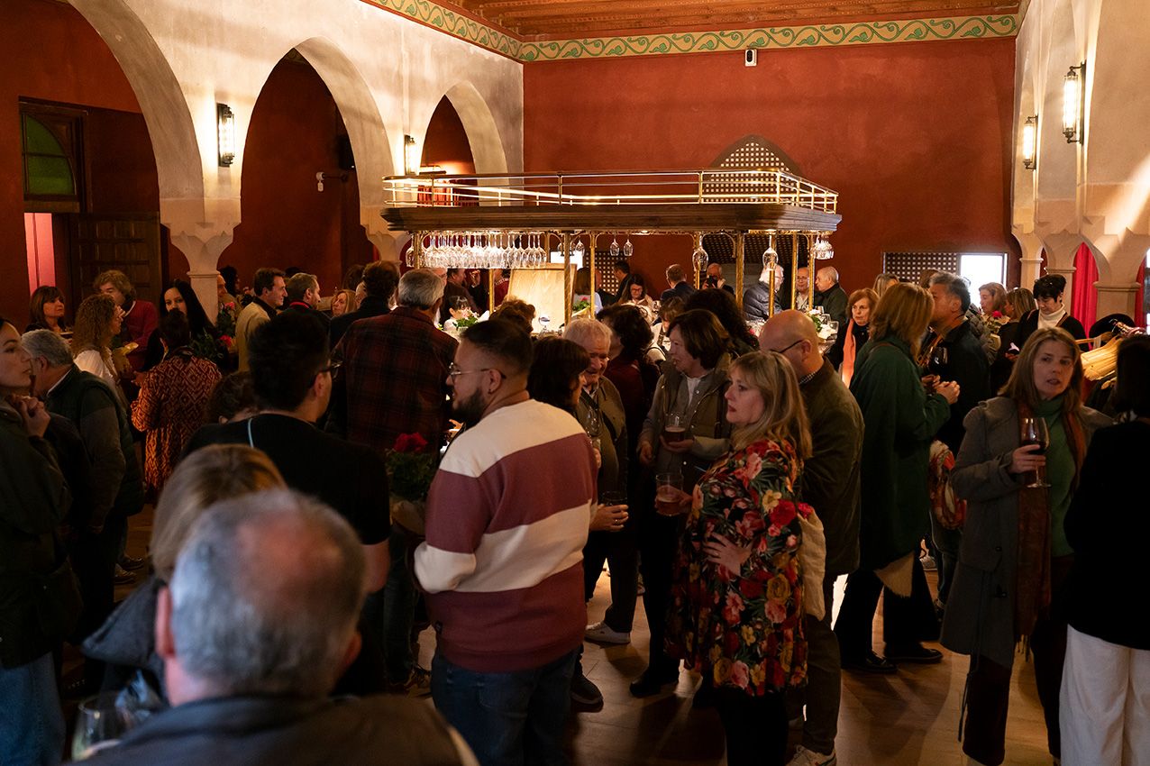 Guests socialize at a lively evening gathering inside a rustic red-walled venue with arched windows.