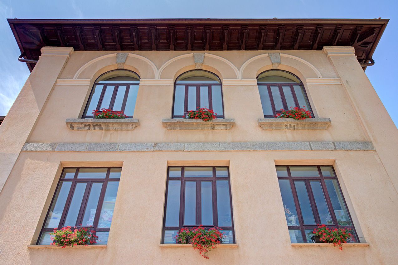 Elegant building facade with arched windows adorned with red flower boxes against a blue sky.