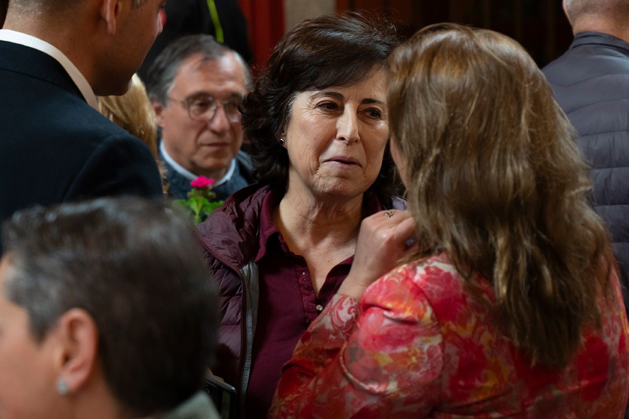 Woman in burgundy top engaged in conversation at a crowded indoor social event.