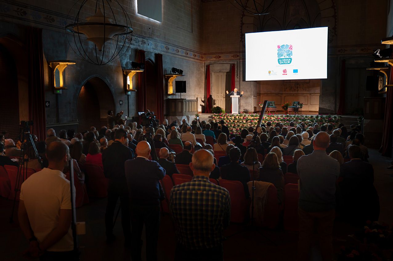 Large audience gathered in a grand hall watching a presentation on a large screen.