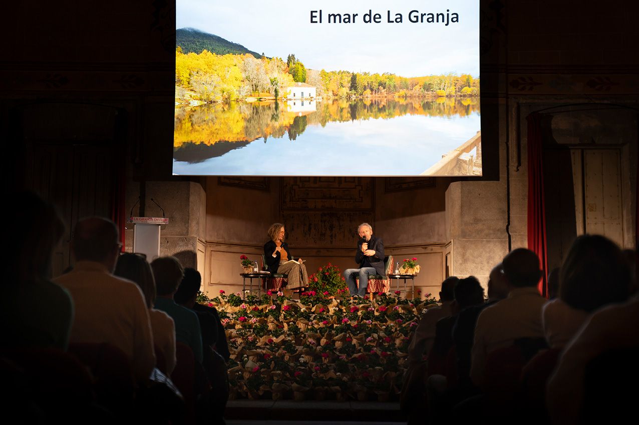 Two speakers on stage with El mar de La Granja projected on screen before an audience.