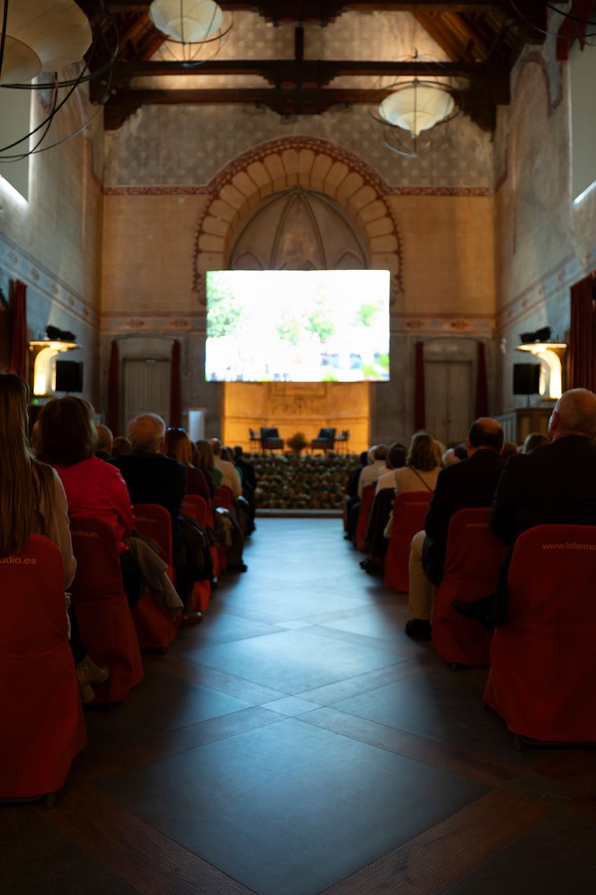 Large audience seated in ornate historic hall watching a presentation on a large projection screen.