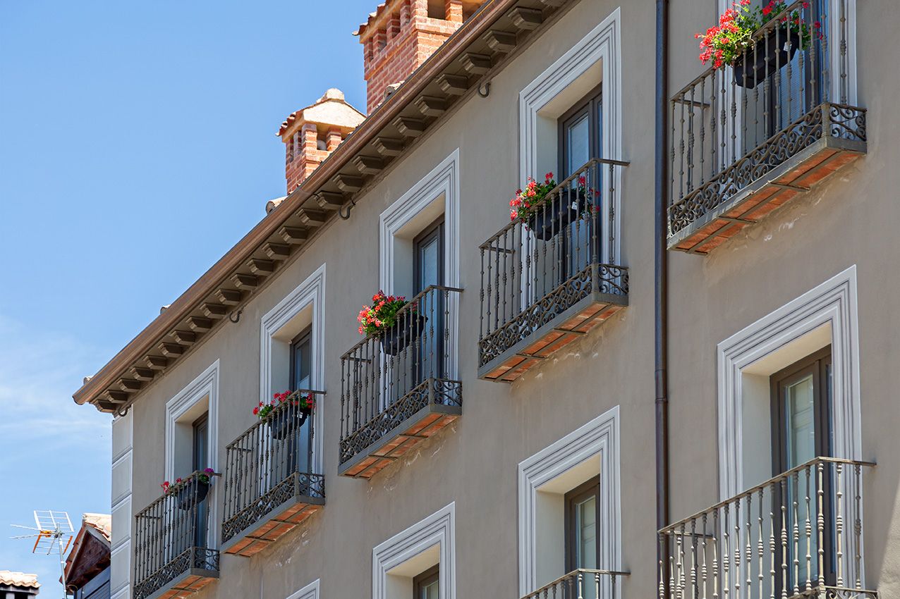 Historic European building facade with ornate balconies adorned with colorful flower boxes against a clear blue sky.