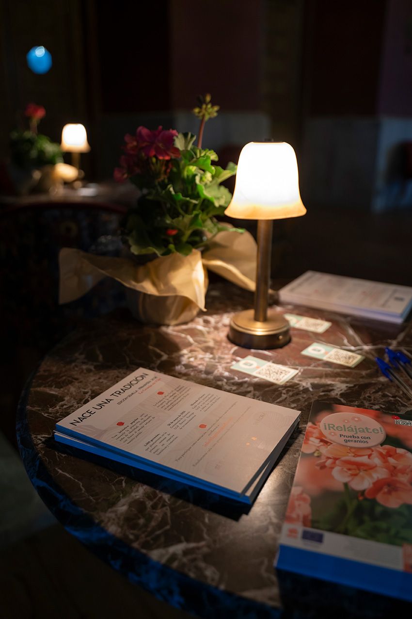 Elegant table with glowing lamp, flower arrangement, menus and brochures in dimly lit venue.