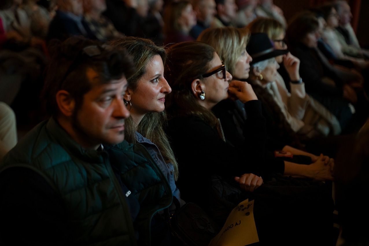 Engaged audience members listen attentively during a cultural conference event in a dimly lit venue.