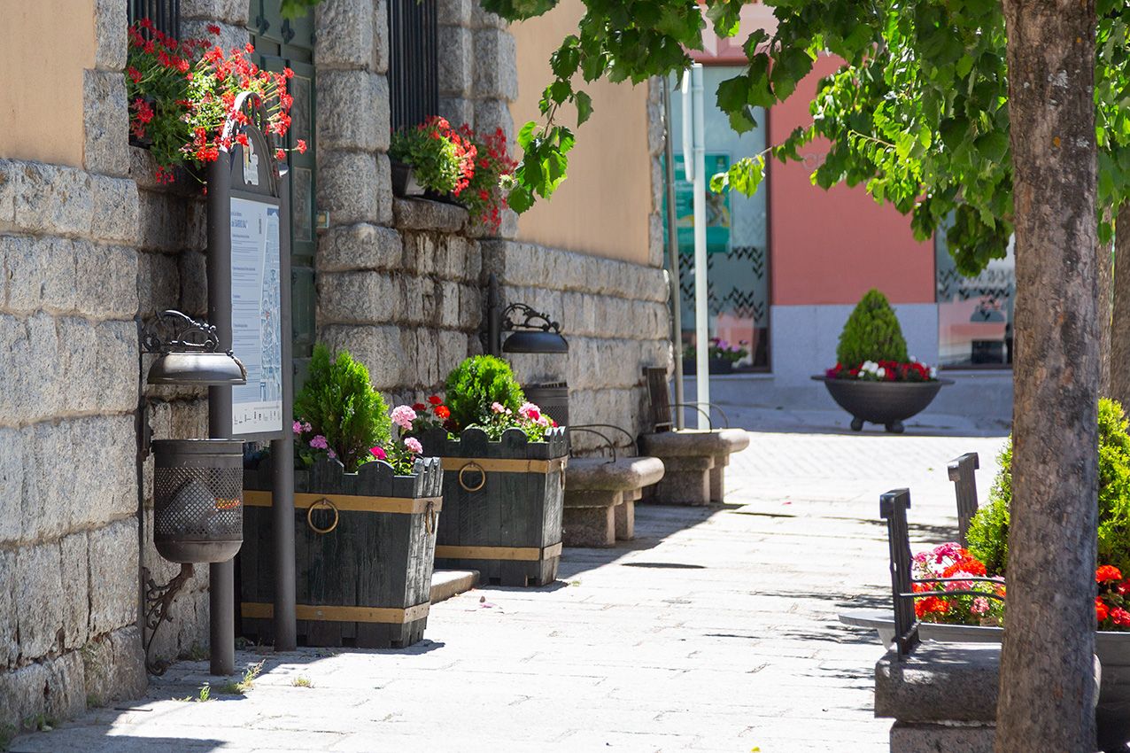 Charming European cobblestone street with colorful flower planters and hanging baskets outside a stone building.