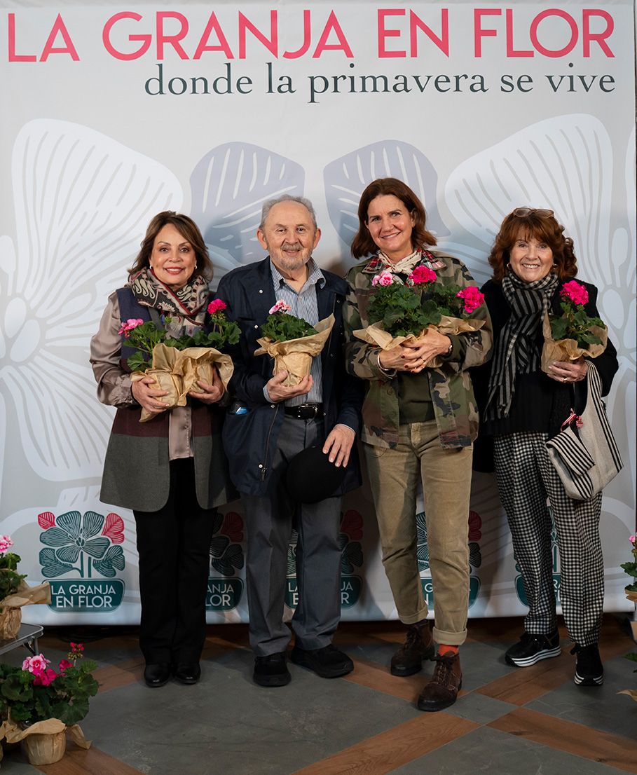 Four people posing with flower bouquets in front of La Granja en Flor spring event banner.