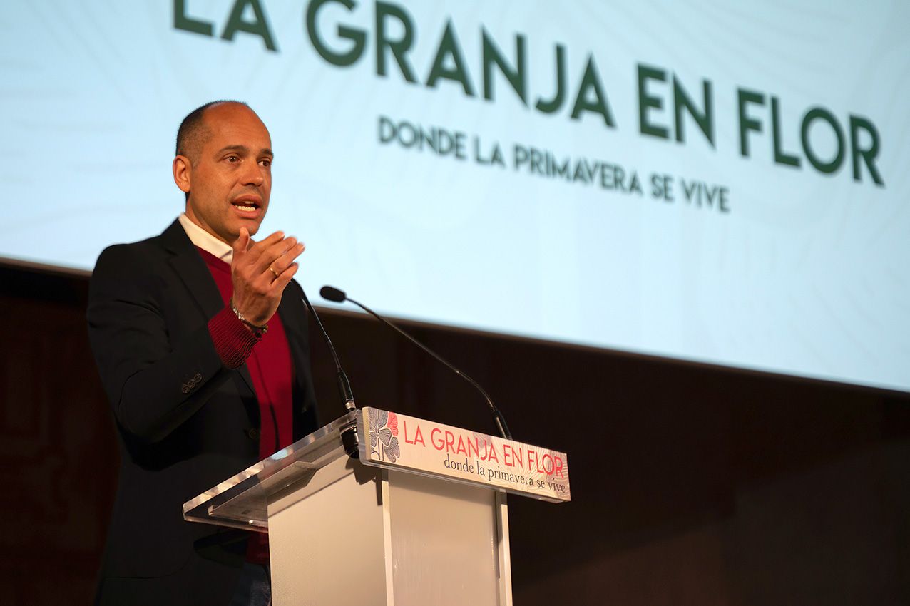 Man in burgundy shirt speaking at a podium at La Granja en Flor spring festival.