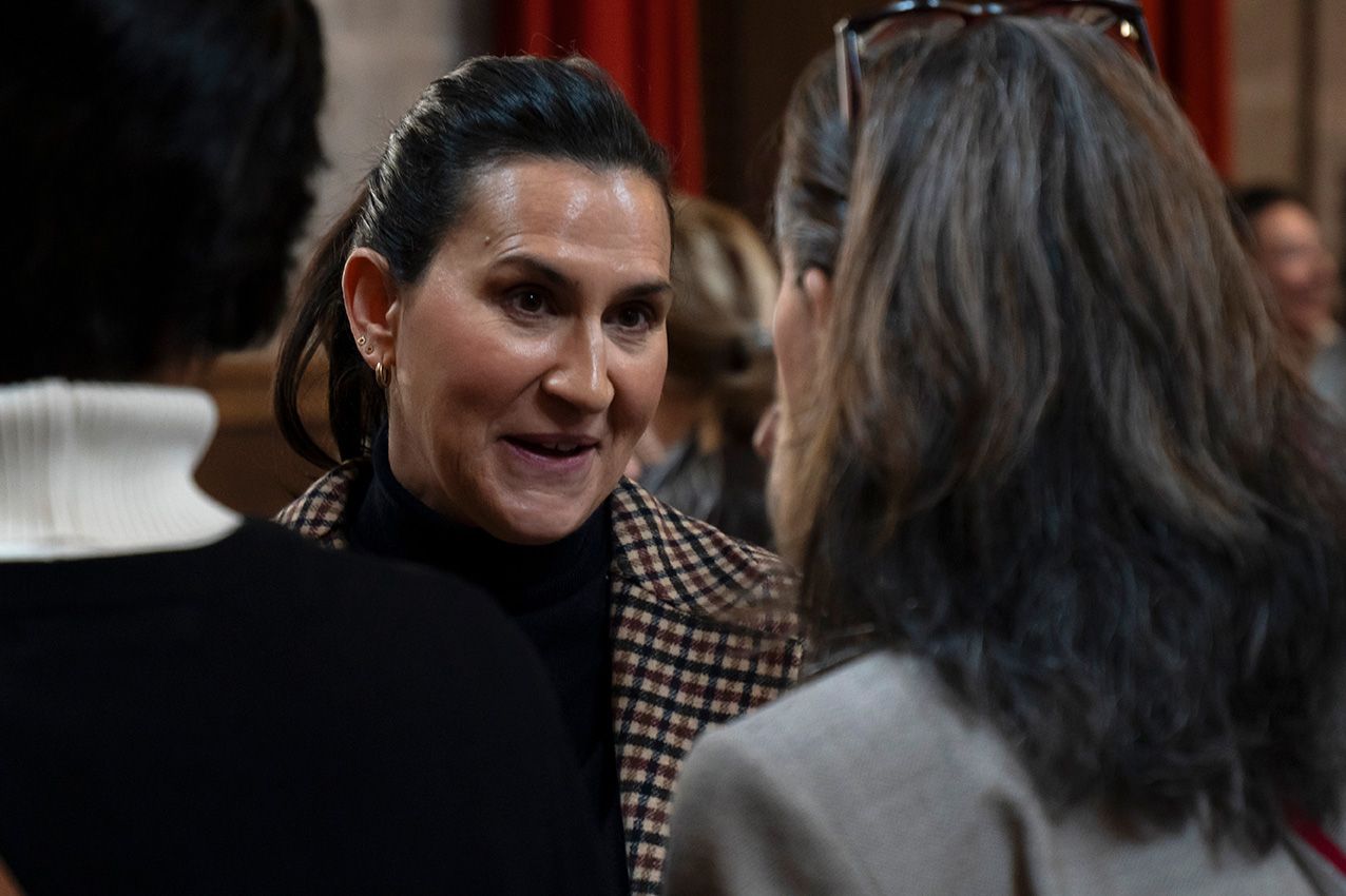 Woman in black turtleneck smiling and conversing at an indoor social gathering event.