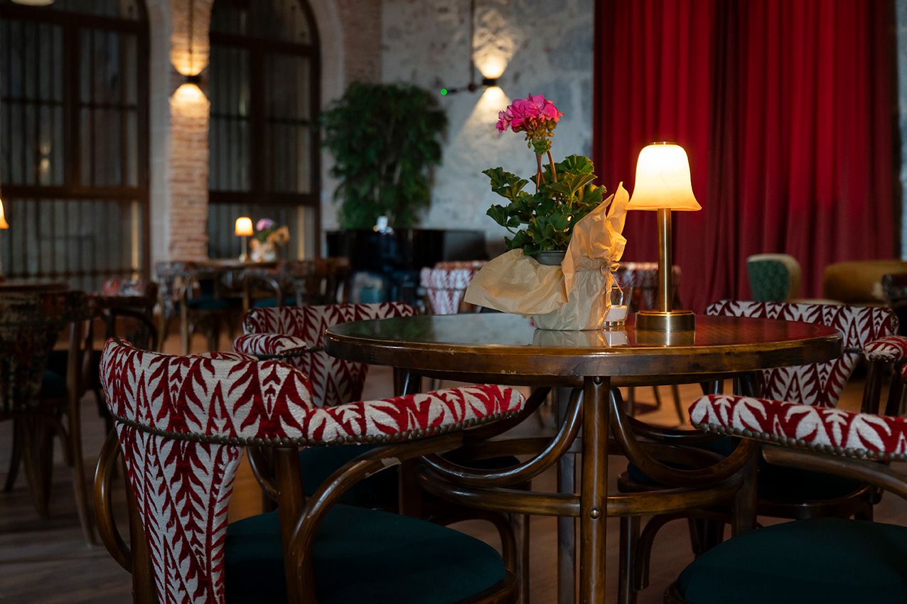 Elegant restaurant interior with patterned chairs, warm lamp, and pink flower centerpiece.