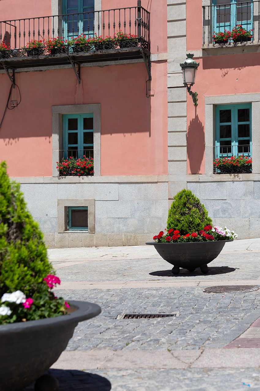Colorful pink building with teal windows and flower-filled planters on a sunny cobblestone plaza.