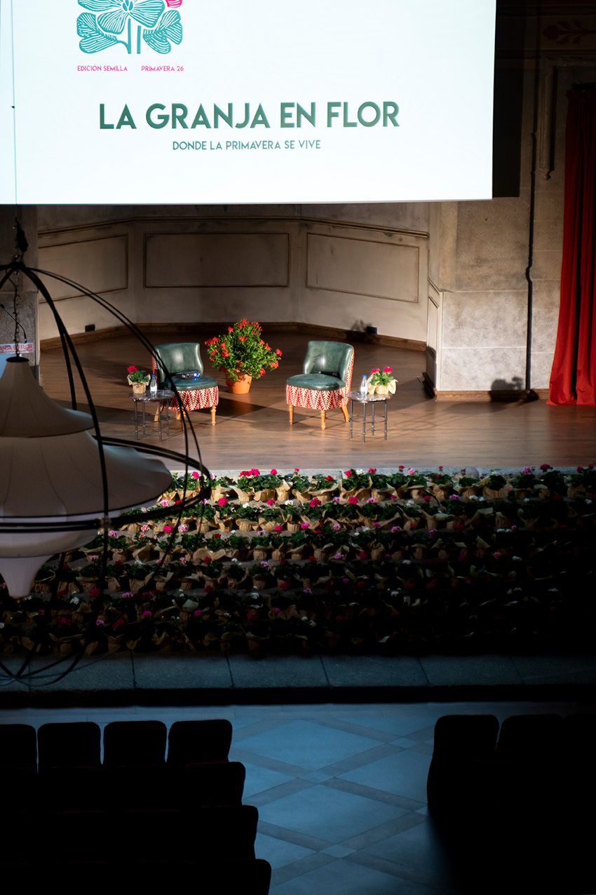 La Granja en Flor spring festival stage with two chairs, flower decorations and projected banner.