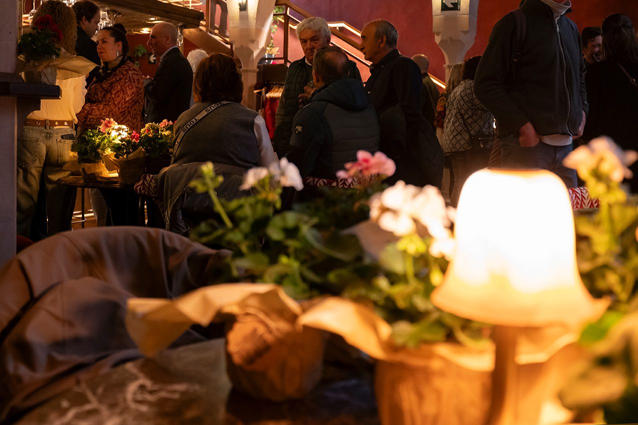 A warmly lit social gathering with guests mingling among pink flowers and glowing candles on tables.