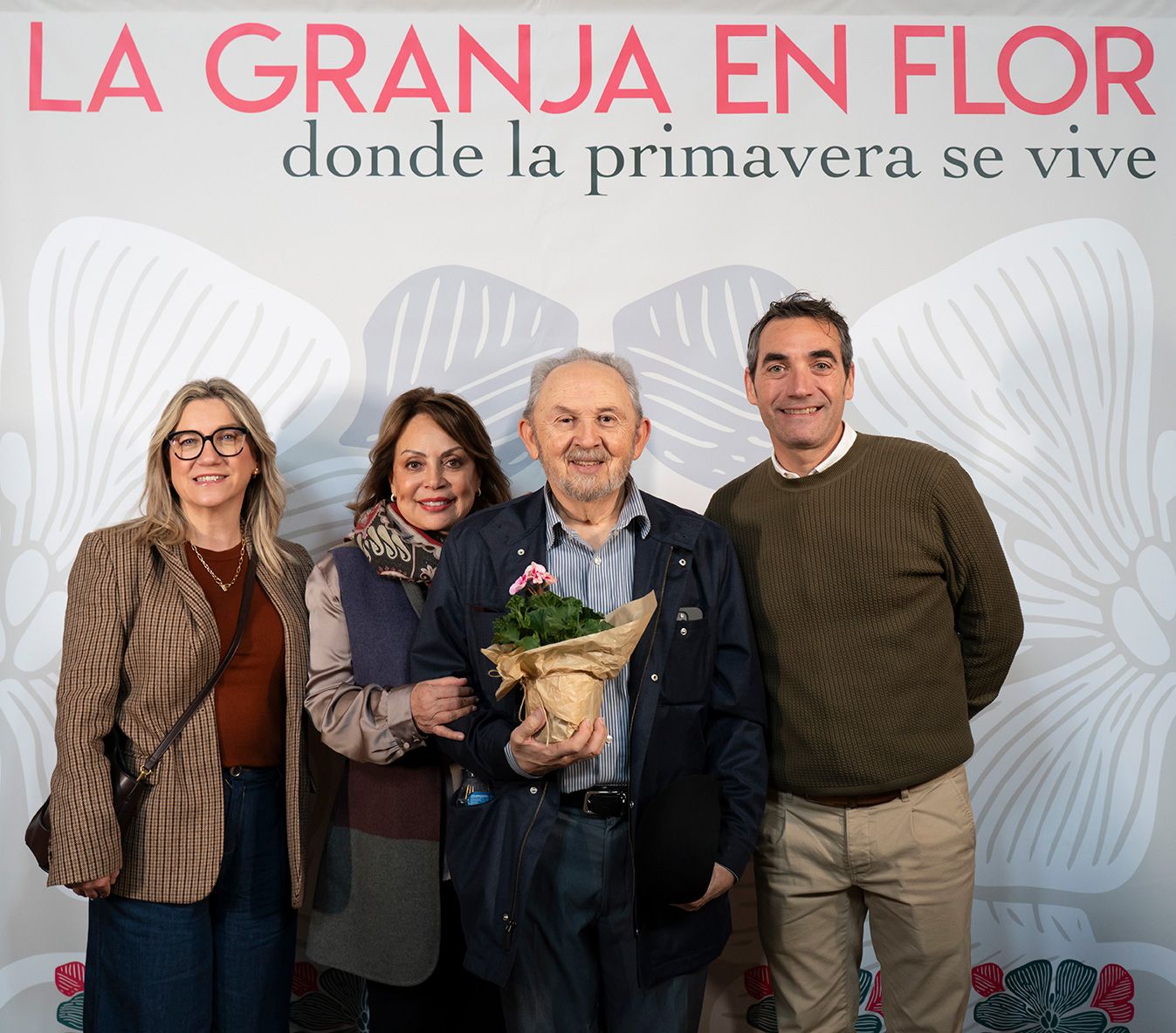 Four people smiling together holding a pink flower pot at La Granja en Flor spring event.